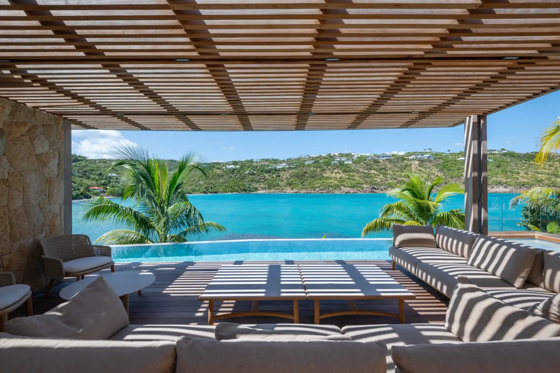 Pool deck under a wood pergola overlooking the lagoon at a luxury St. Barth villa